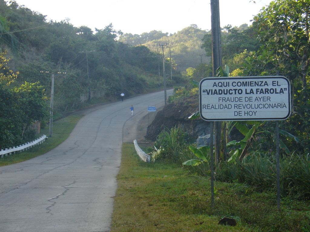 Auf diesem Schild steht 'Hier beginnt die Straße 'Die Fackel', Betrug von gestern, revolutionäre Wirklichkeit von heute'.<br />Bis Anfang der sechziger Jahre war Baracoa vom restlichen Kuba abgeschnitten und nur per Schiff erreichbar, denn es gab keine Straße durch die Berge. Die kubanische Regierung hatte in den fünfziger Jahren eine Straße versprochen, aber nicht gebaut. Bald nach der Revolution wurde sie dann tatsächlich gebaut.