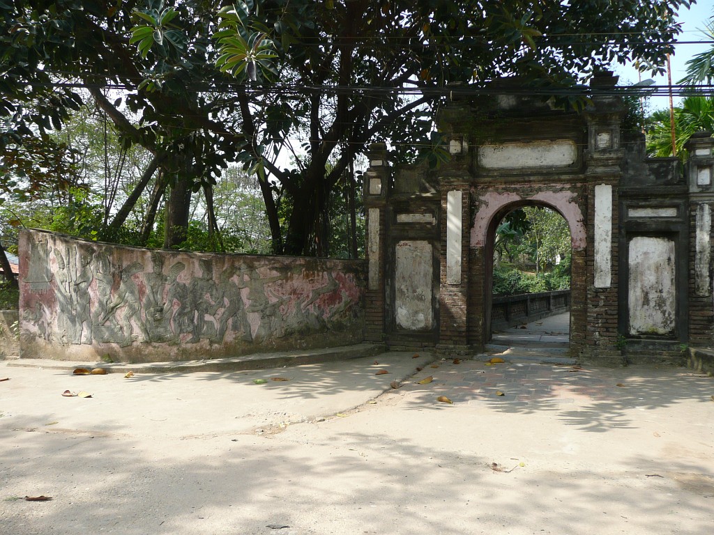 Ins Zentrum von Co Loa führt ein Tor. An der Mauer davor sieht man Szenen aus dem Leben der Ureinwohner Vietnams ...
