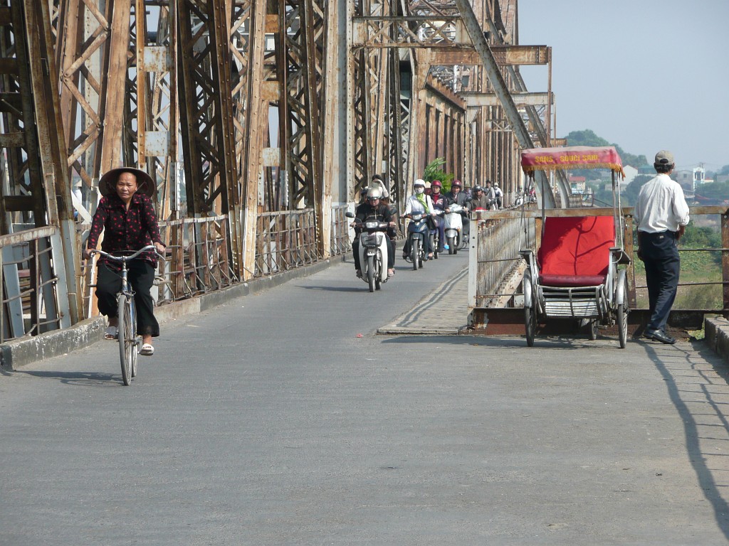 ... Diese Brücke wurde von den französischen Kolonialherren gebaut und war bis in die 80-er Jahre die einzige Brücke über den Roten Fluss in Hanoi. An dieser Stelle ist der Radstreifen verbreitert. Normalerweise ist er so schmal wie man es links vom Rikscha sieht.